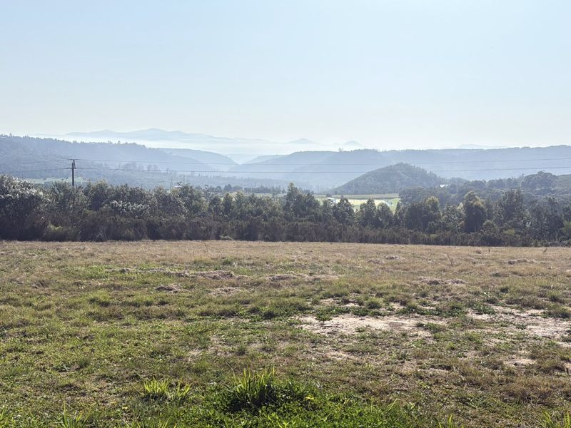 A scenic view overlooking a vast, open grassy landscape with rolling hills and distant mountains in the background.