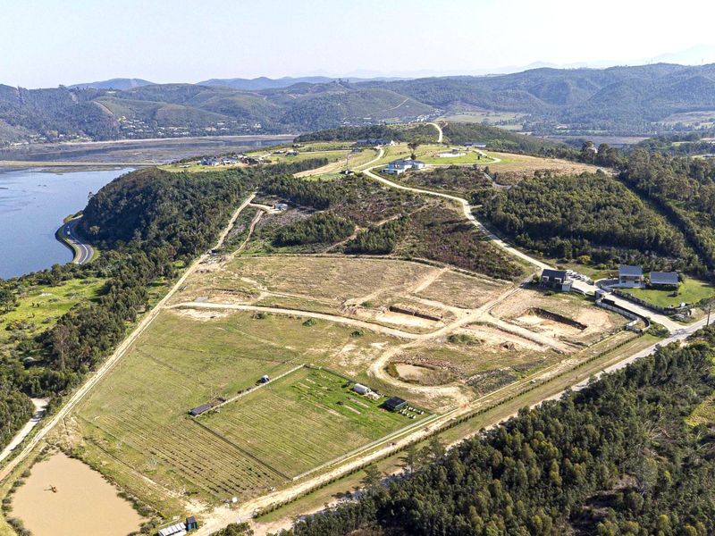 Aerial view of a large residential development site featuring graded plots, internal road infrastructure, and scenic views of the surrounding landscape and water.