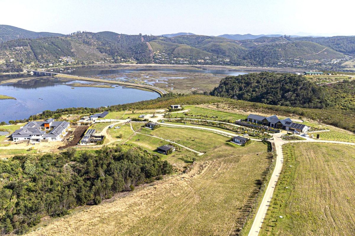 An expansive aerial view of a residential estate featuring multiple dwellings, solar installations, and scenic landscape views overlooking the nearby estuary and hills.