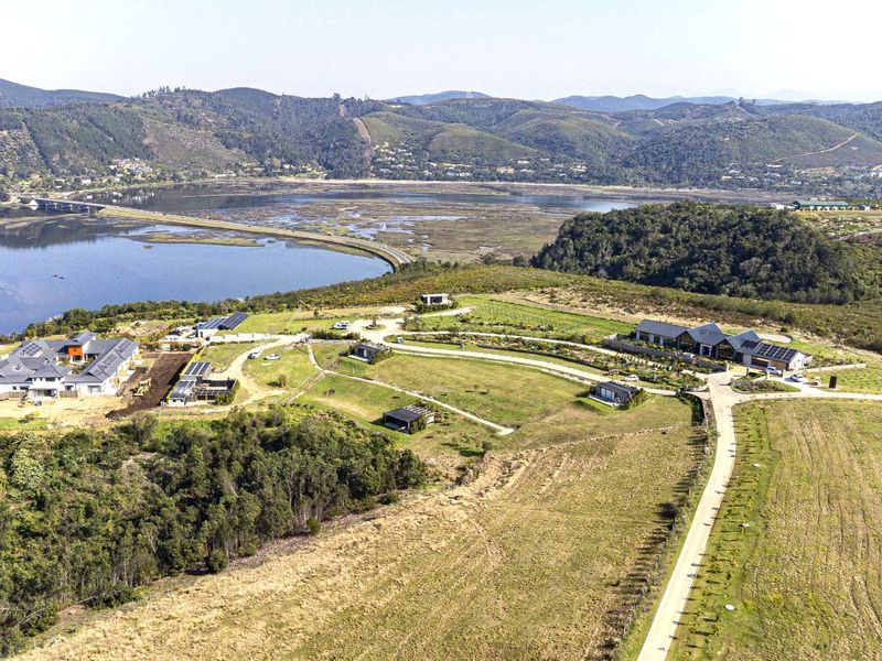 An expansive aerial view of a residential estate featuring multiple dwellings, solar installations, and scenic landscape views overlooking the nearby estuary and hills.