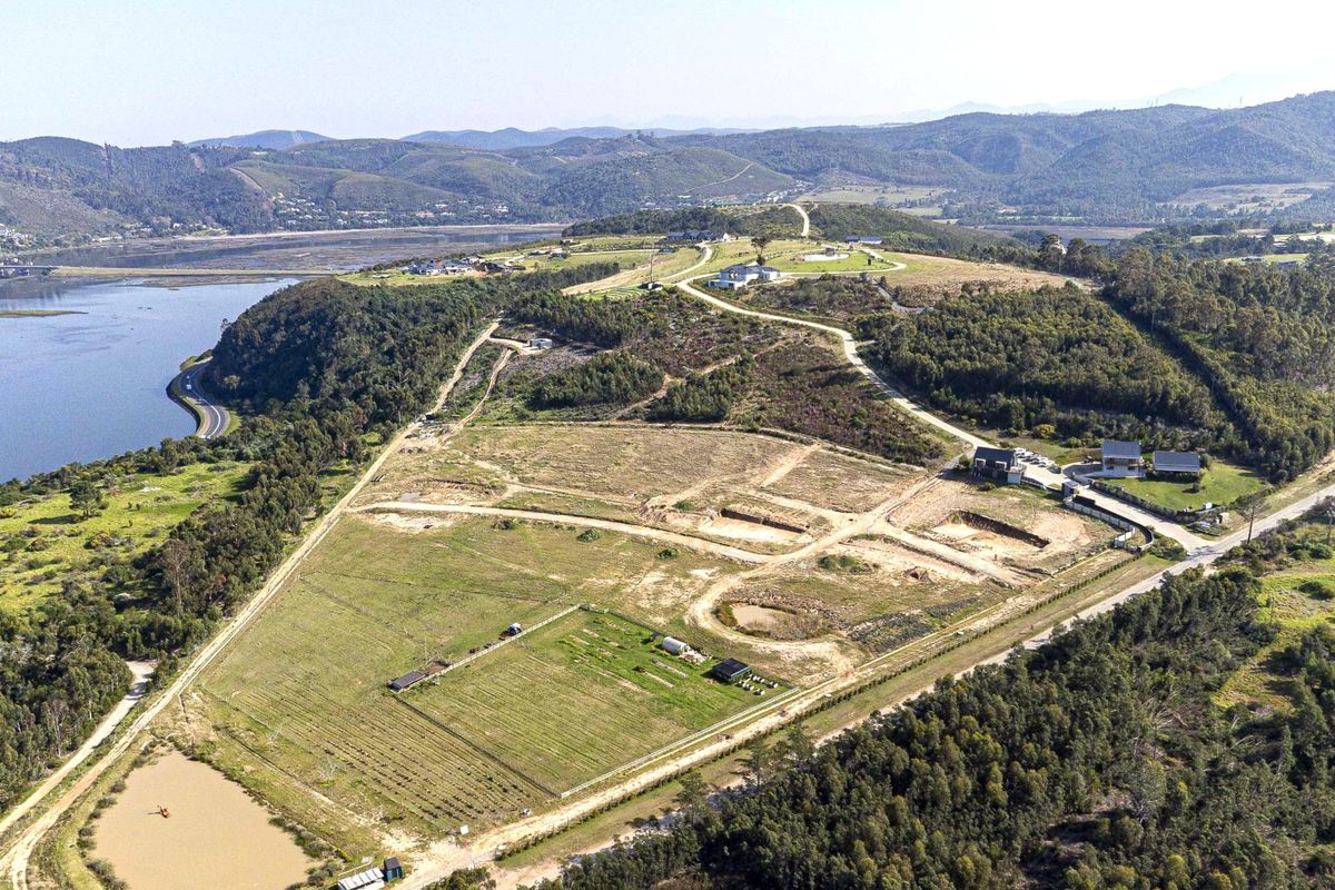 Aerial view of a large residential development site featuring graded plots, internal road infrastructure, and scenic views of the surrounding landscape and water.
