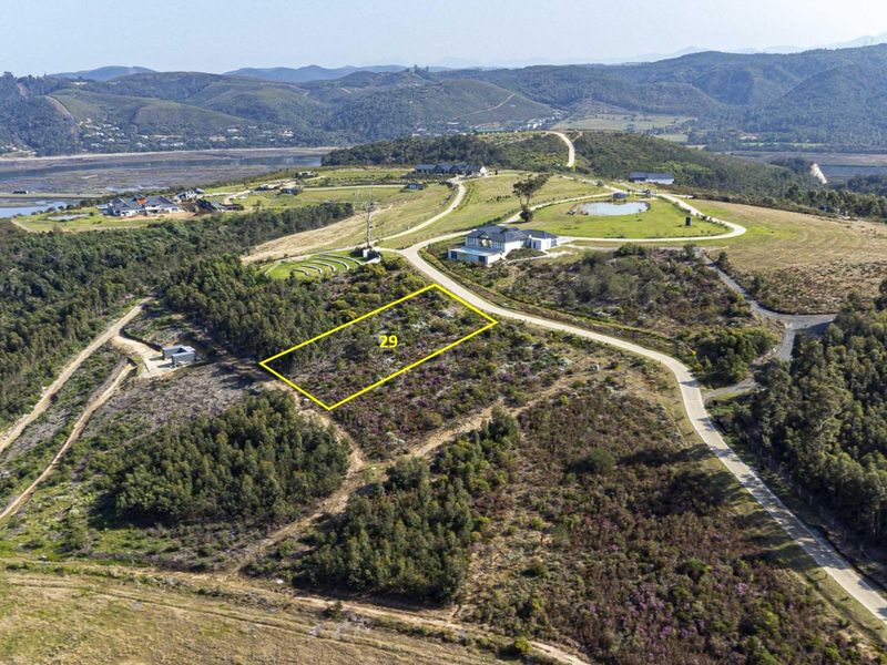 Aerial view of a vacant residential plot in a scenic estate, featuring natural vegetation and access to paved estate roads.