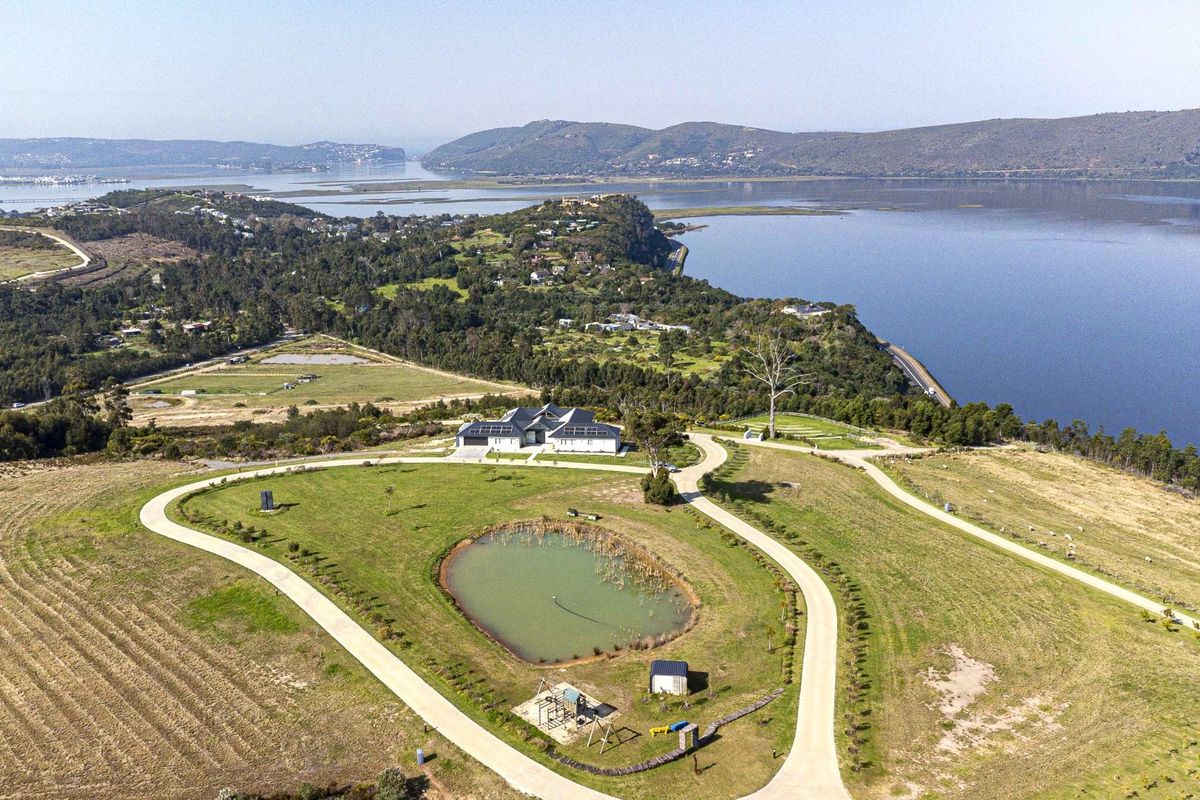 Aerial view of a residential property featuring a large plot of land, a private pond, paved driveway, and a house equipped with solar panels.