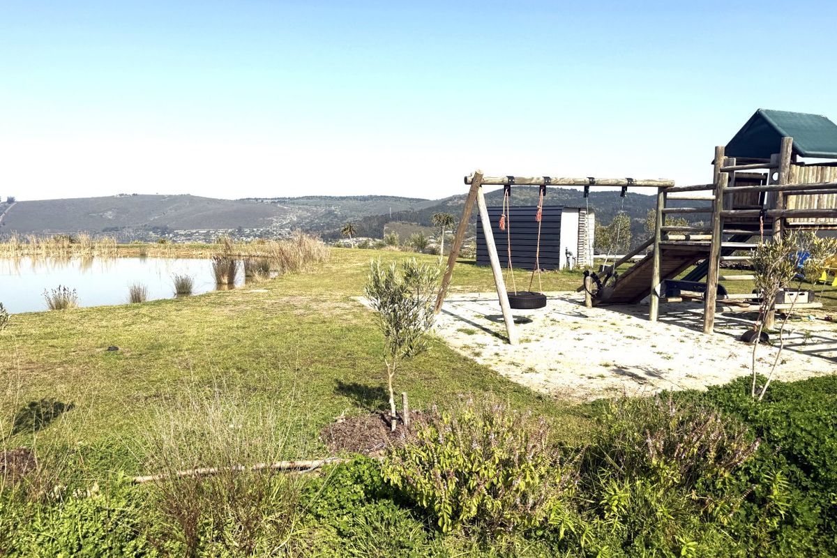 A spacious outdoor garden area featuring a natural pond, a wooden playground structure, and a small storage shed with scenic landscape views.