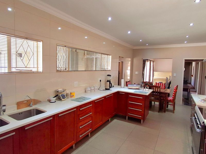 A well-maintained kitchen featuring warm-toned wooden cabinetry, stone countertops, a double sink, and integrated appliances, with an open-plan flow to the dining area.
