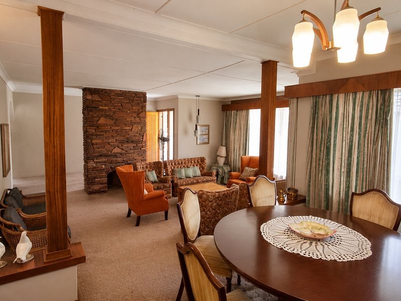 Spacious open-plan living and dining area featuring a prominent stone fireplace, timber support columns, and neutral wall finishes.