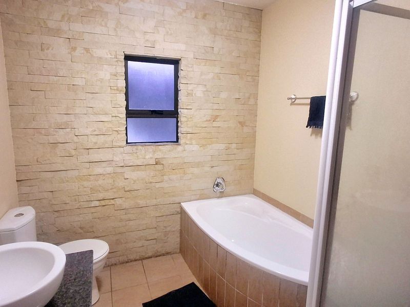 A clean bathroom featuring a built-in bathtub, a stone-clad feature wall, a separate shower enclosure, and a vanity basin.