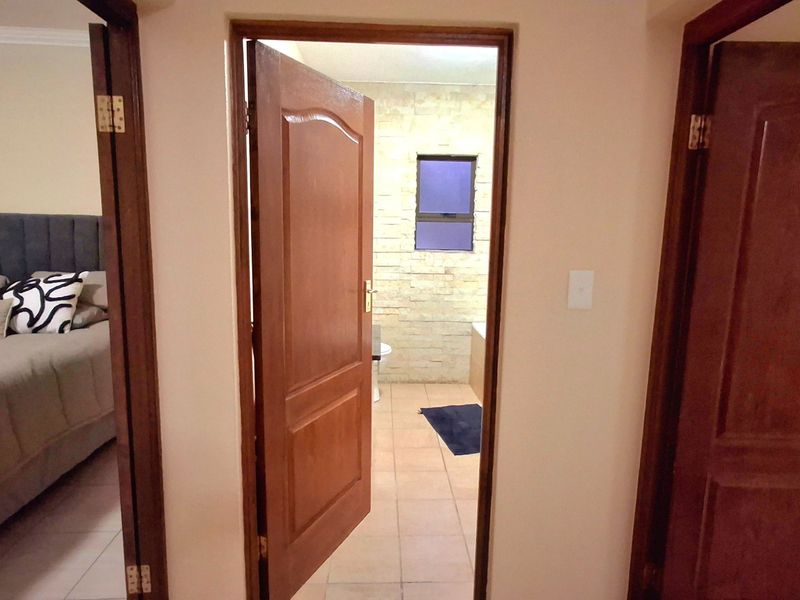 A hallway view showing access to a bedroom and a bathroom with stone-clad feature wall and tiled flooring.