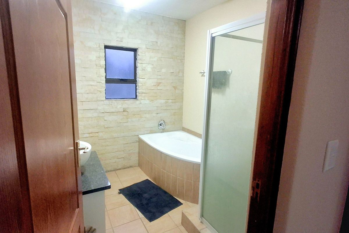 A functional bathroom featuring a built-in bathtub, separate shower enclosure, and a decorative stone-clad feature wall.