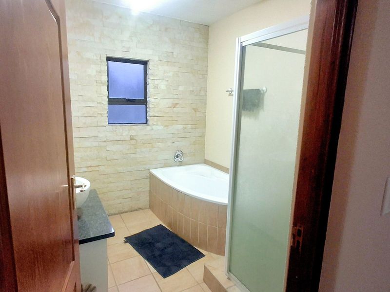 A functional bathroom featuring a built-in bathtub, separate shower enclosure, and a decorative stone-clad feature wall.