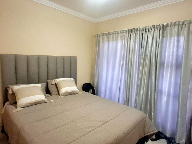 A standard bedroom featuring neutral wall tones, coving, and a large window covered by curtains.