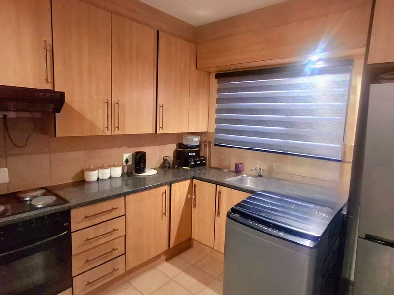 Functional kitchen featuring wood-look laminate cabinetry, granite countertops, built-in oven, electric hob, and a tiled backsplash.