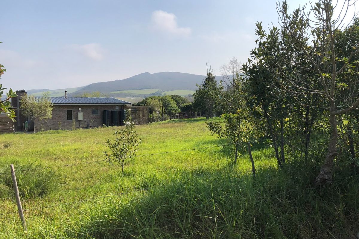 A view of a residential property featuring a brick dwelling, water storage tanks, and surrounding grassy land with mountain views in the background.