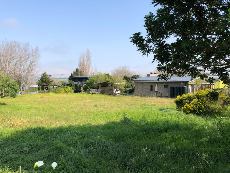 A view of a residential property featuring a brick dwelling, water storage tanks, and a wooden carport set within a spacious grassy garden area.