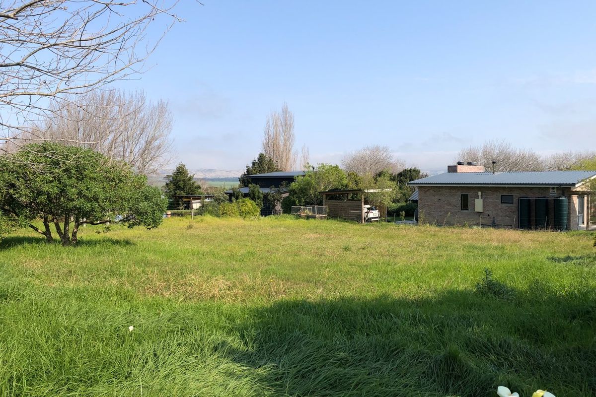 A view of the rear yard featuring a brick residential building, metal roofing, water storage tanks, and a carport set within a grassy landscape.