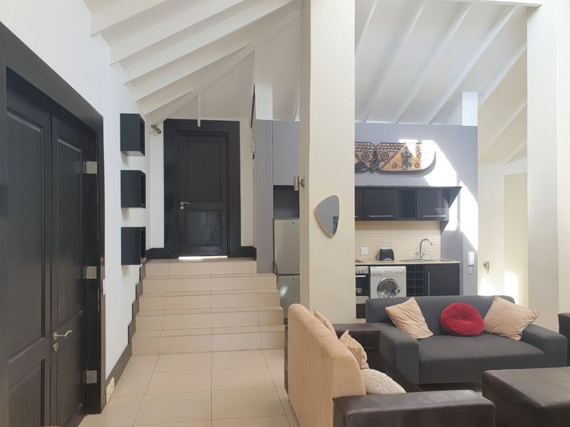 Open-plan living area featuring a vaulted ceiling, tiled floors, and a compact kitchen with built-in cabinetry and appliances.