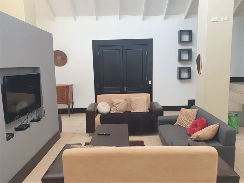 A spacious living room featuring a vaulted ceiling, tiled flooring, and a modern recessed media wall with double door access.