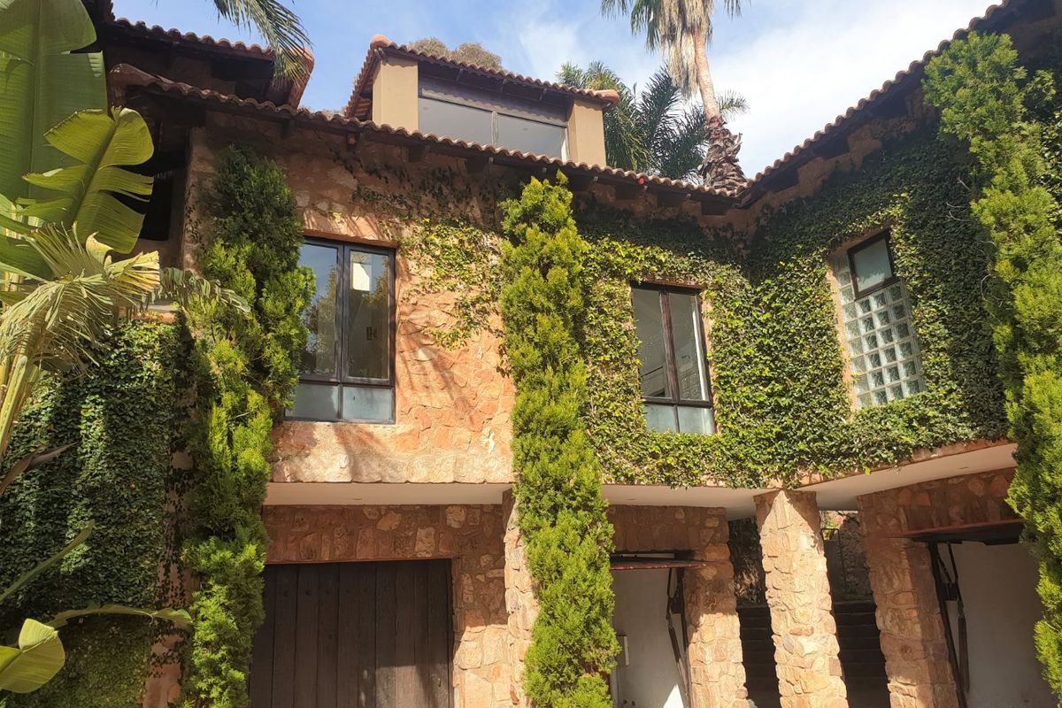 A rustic exterior view of the property featuring stone cladding, terracotta roof tiles, and lush climbing greenery on the facade.