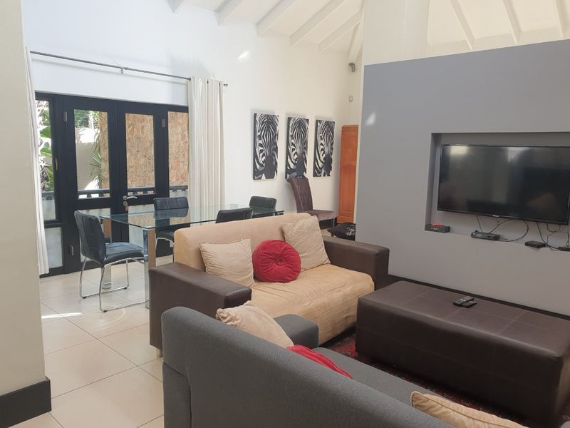 Open plan living and dining area featuring vaulted ceilings, tiled flooring, and a recessed media wall with direct access to an outdoor patio.