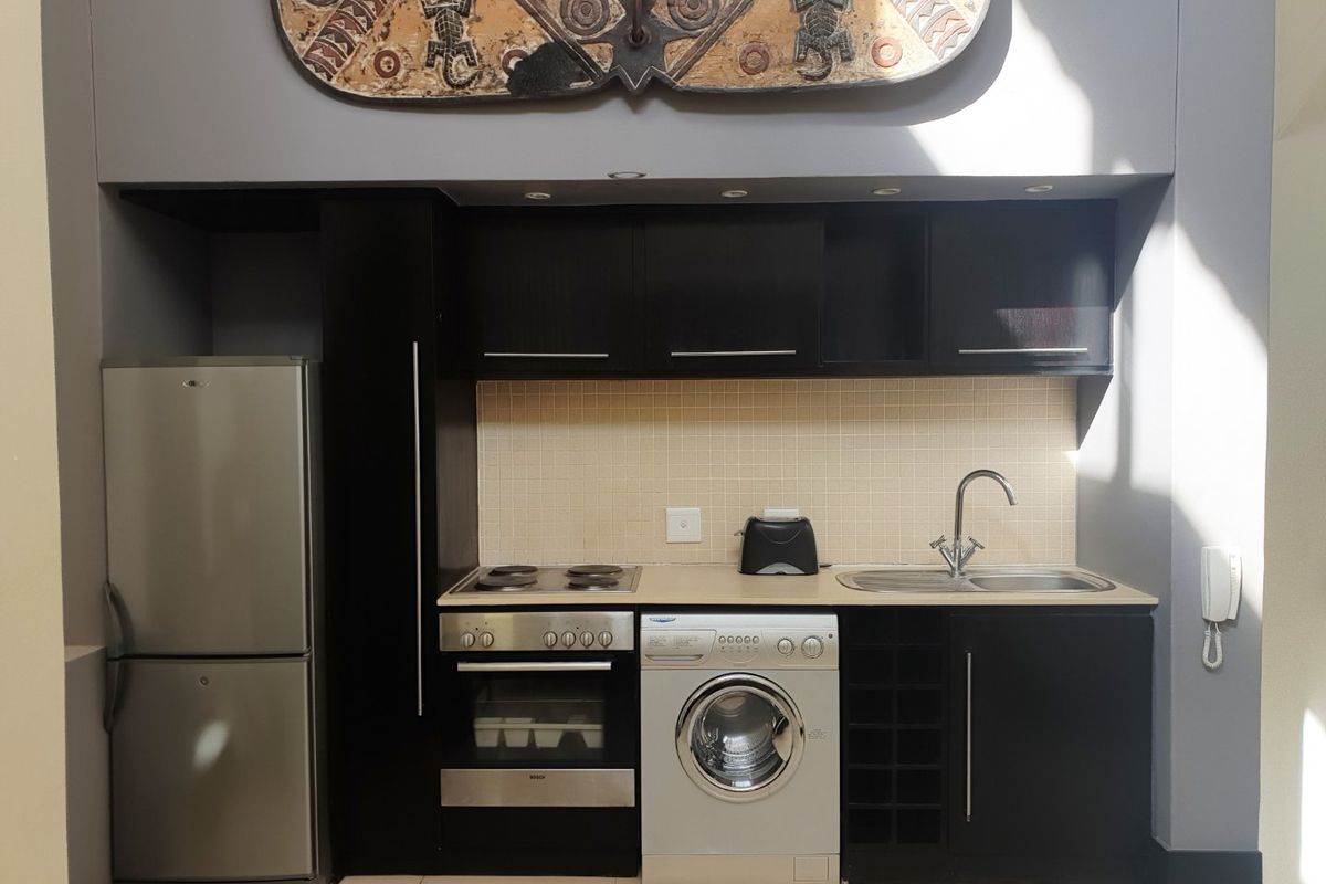 Compact kitchen featuring dark cabinetry, tiled backsplash, built-in oven, electric hob, and integrated sink with modern mixer tap.