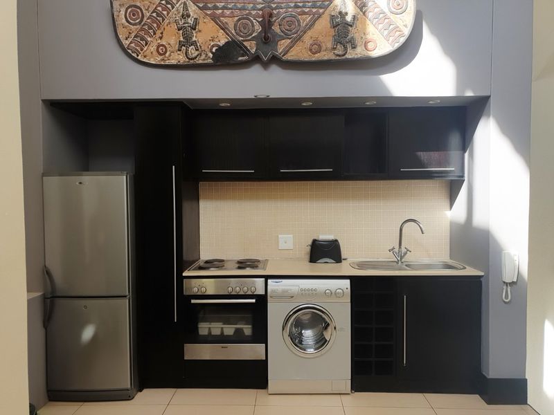 Compact kitchen featuring dark cabinetry, tiled backsplash, built-in oven, electric hob, and integrated sink with modern mixer tap.