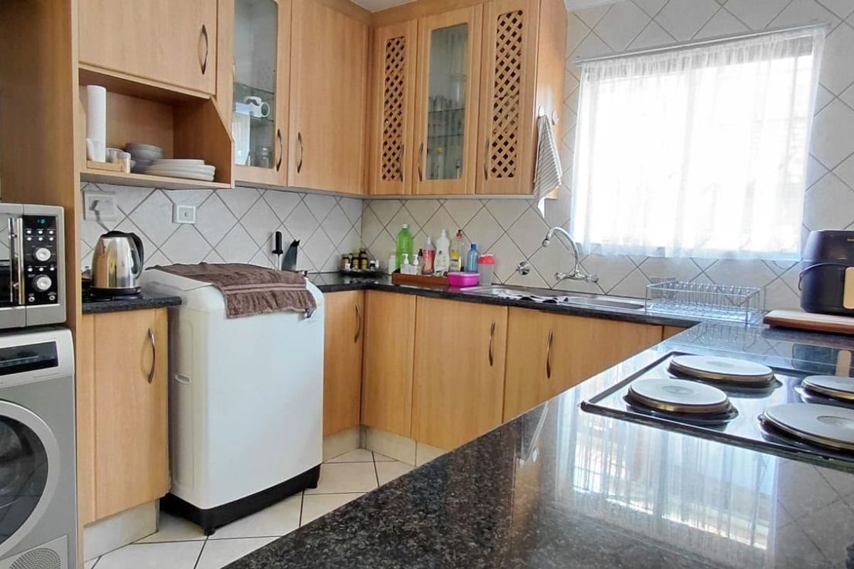 A functional kitchen featuring wooden cabinetry, granite countertops, a tiled backsplash, and an integrated electric hob, offering practical workspace and storage.