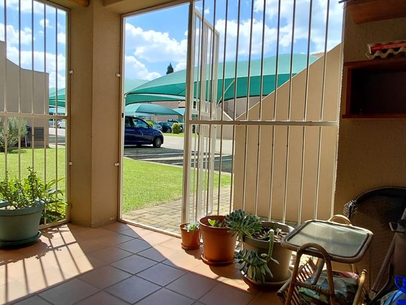 A covered patio area featuring tiled flooring, built-in shelving, and a security gate, providing direct access to the garden and complex grounds.