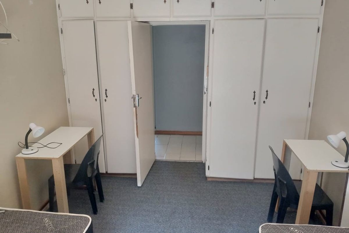 Bedroom featuring extensive built-in cupboard storage and carpeted flooring, offering a functional layout with potential for cosmetic updates.