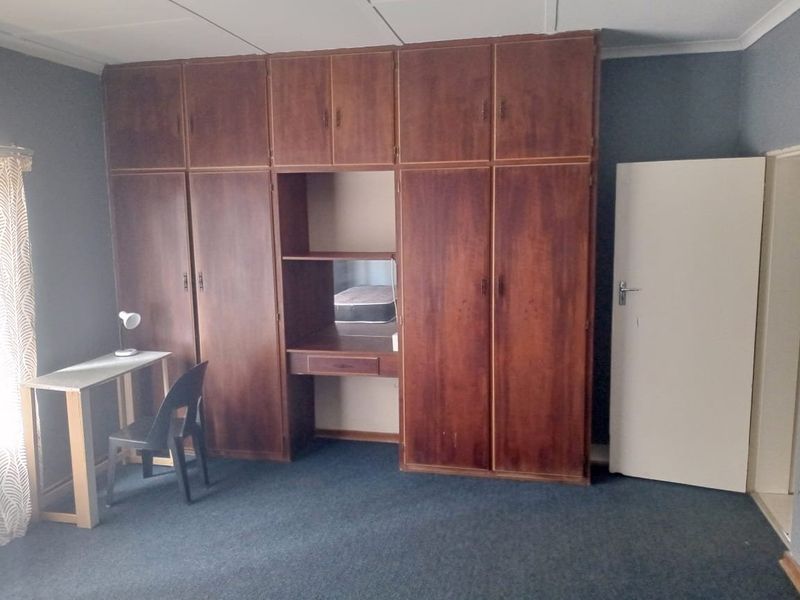 A bedroom featuring extensive built-in wooden cabinetry with an integrated vanity area, carpeted flooring, and standard ceiling tiles.