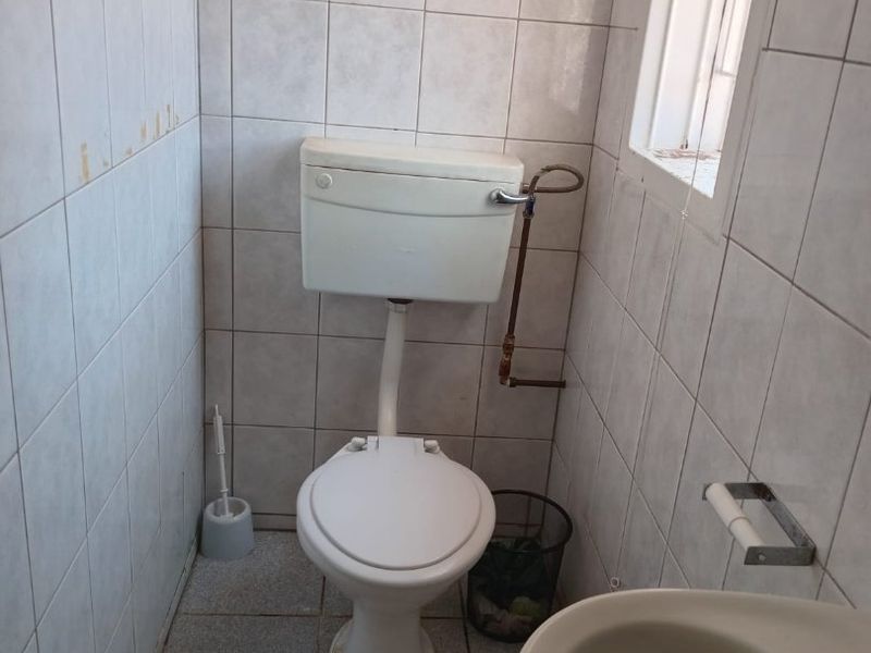 A compact guest bathroom featuring tiled walls and floors, equipped with a standard toilet and basin, requiring cosmetic updates to modernize the space.