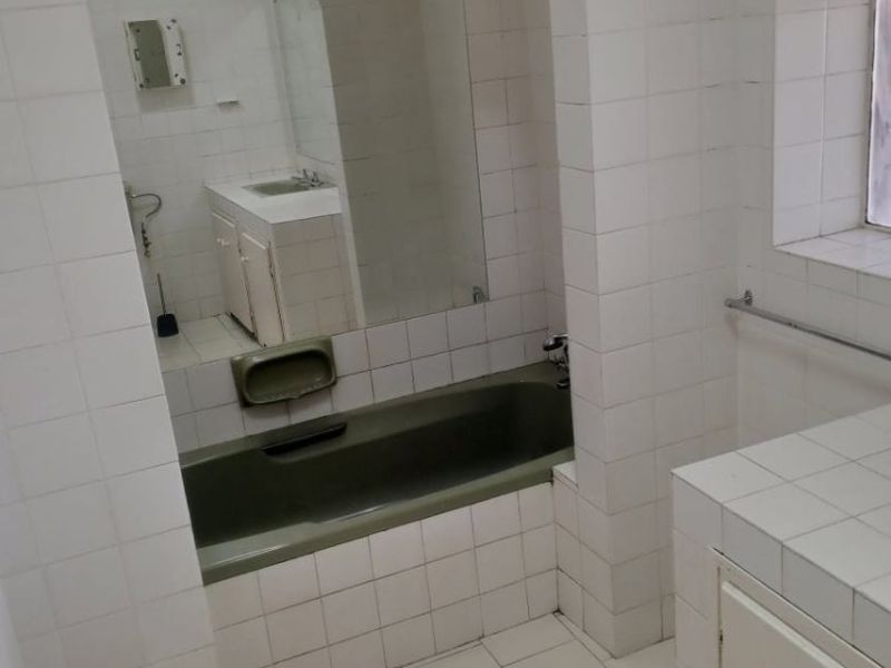 A dated bathroom featuring a built-in bathtub, tiled vanity, and white wall tiles. The space is ready for a modern renovation.