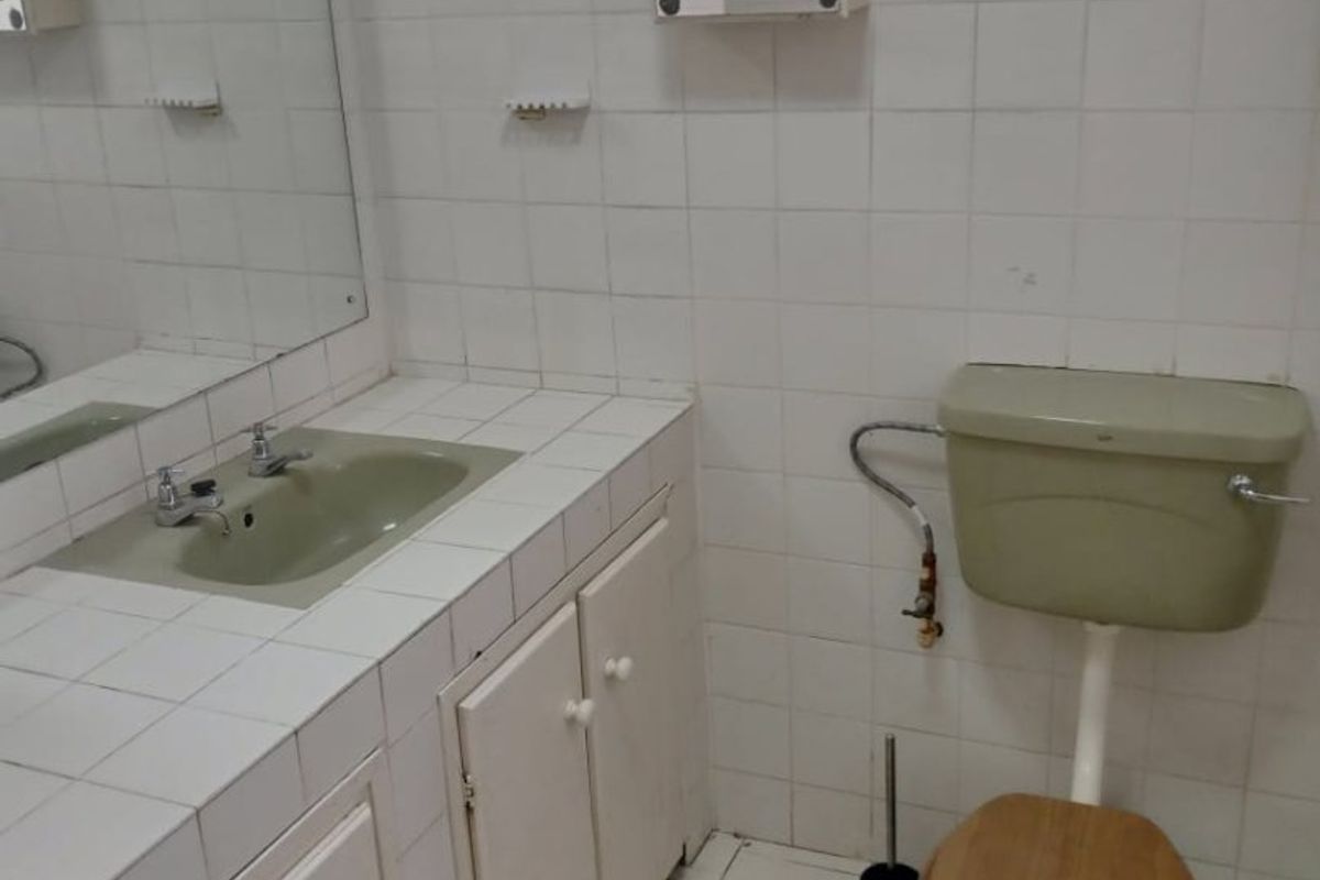 A dated bathroom featuring a tiled vanity with integrated sink, wall-mounted medicine cabinet, and original ceramic toilet suite.