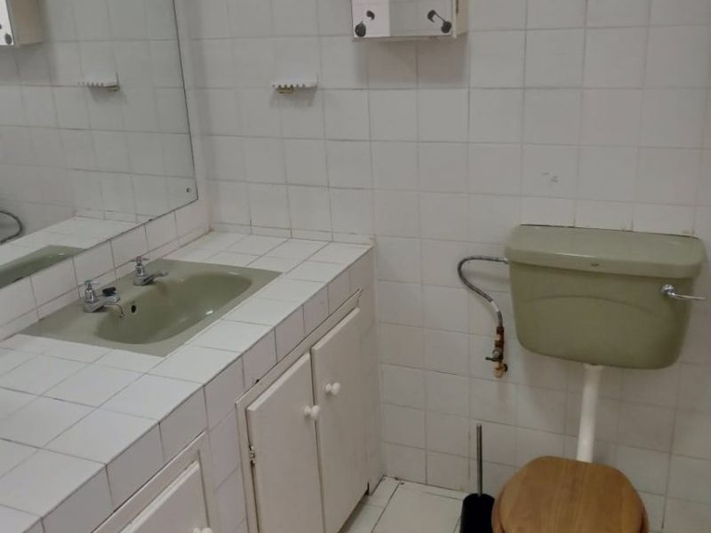 A dated bathroom featuring a tiled vanity with integrated sink, wall-mounted medicine cabinet, and original ceramic toilet suite.