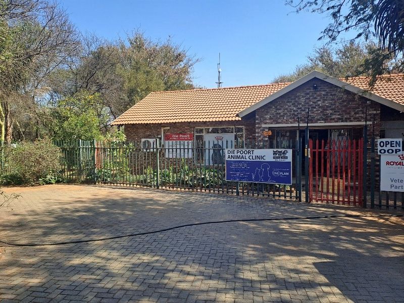 Front exterior view of a brick-faced building with a tiled roof, featuring a paved driveway and secure metal perimeter fencing.