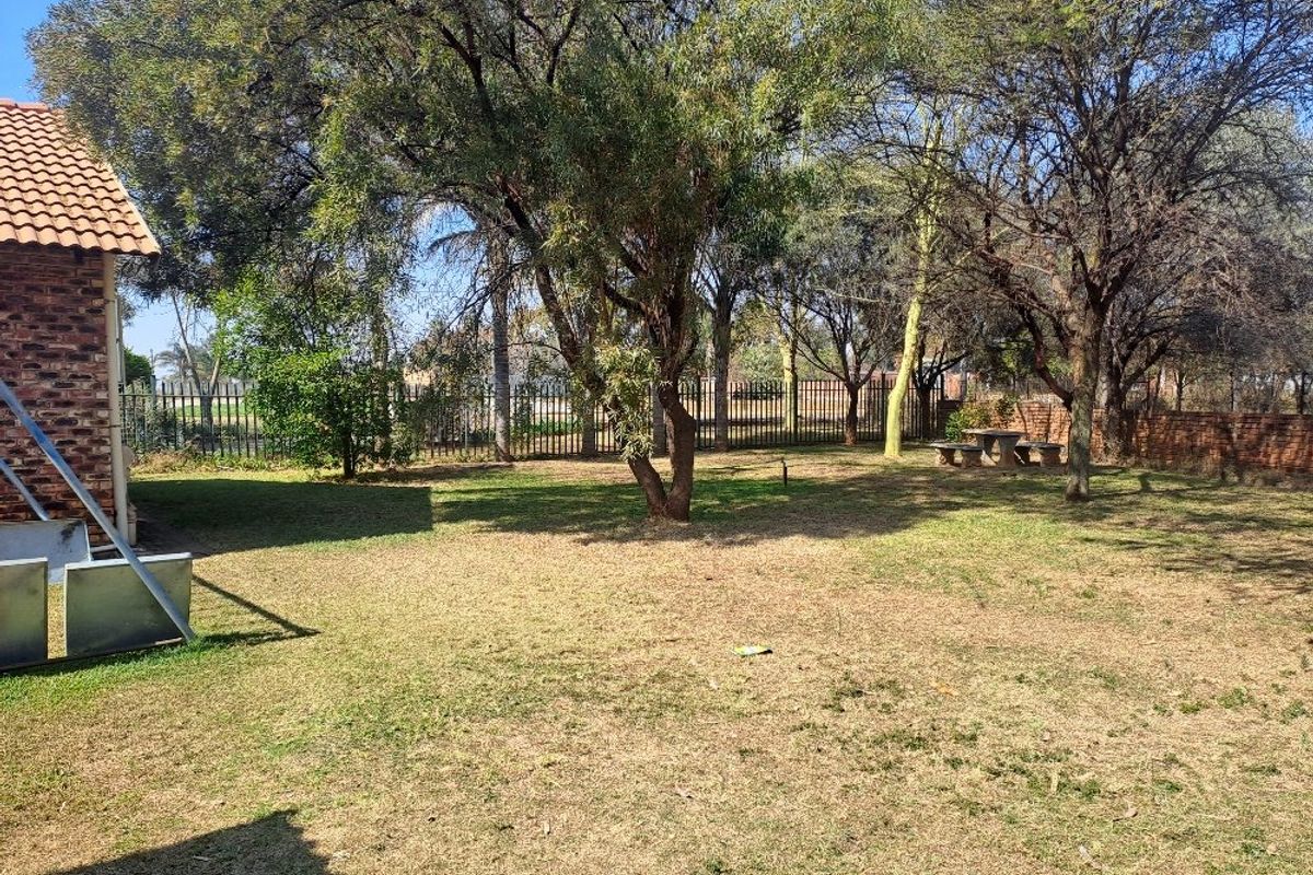 A spacious, well-established garden area featuring mature trees, brick perimeter fencing, and a secure metal boundary fence.