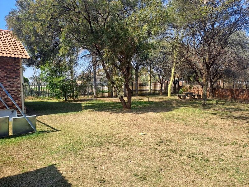A spacious, well-established garden area featuring mature trees, brick perimeter fencing, and a secure metal boundary fence.