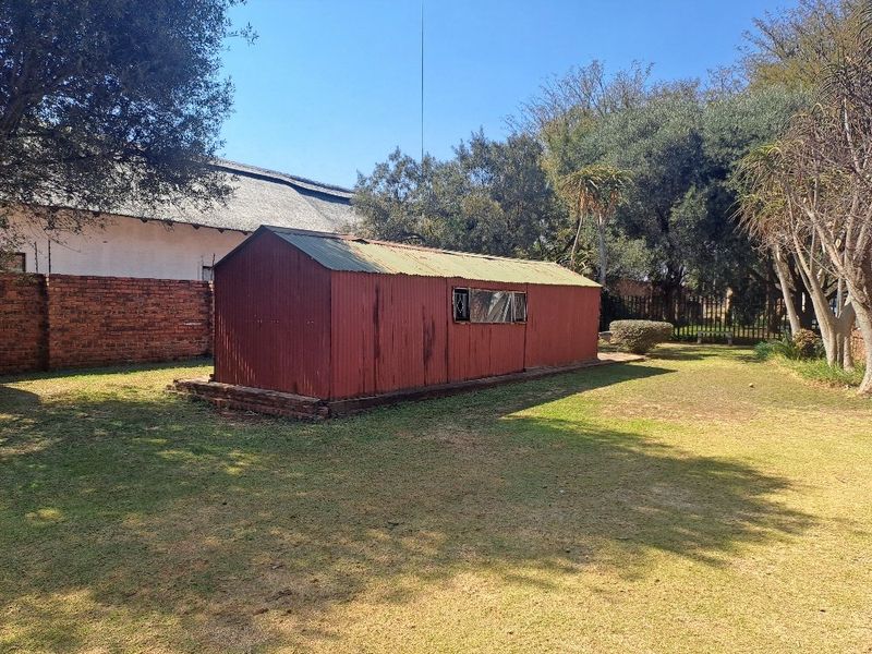 A detached corrugated metal utility shed situated in a spacious garden area, featuring a brick foundation and security-barred window.