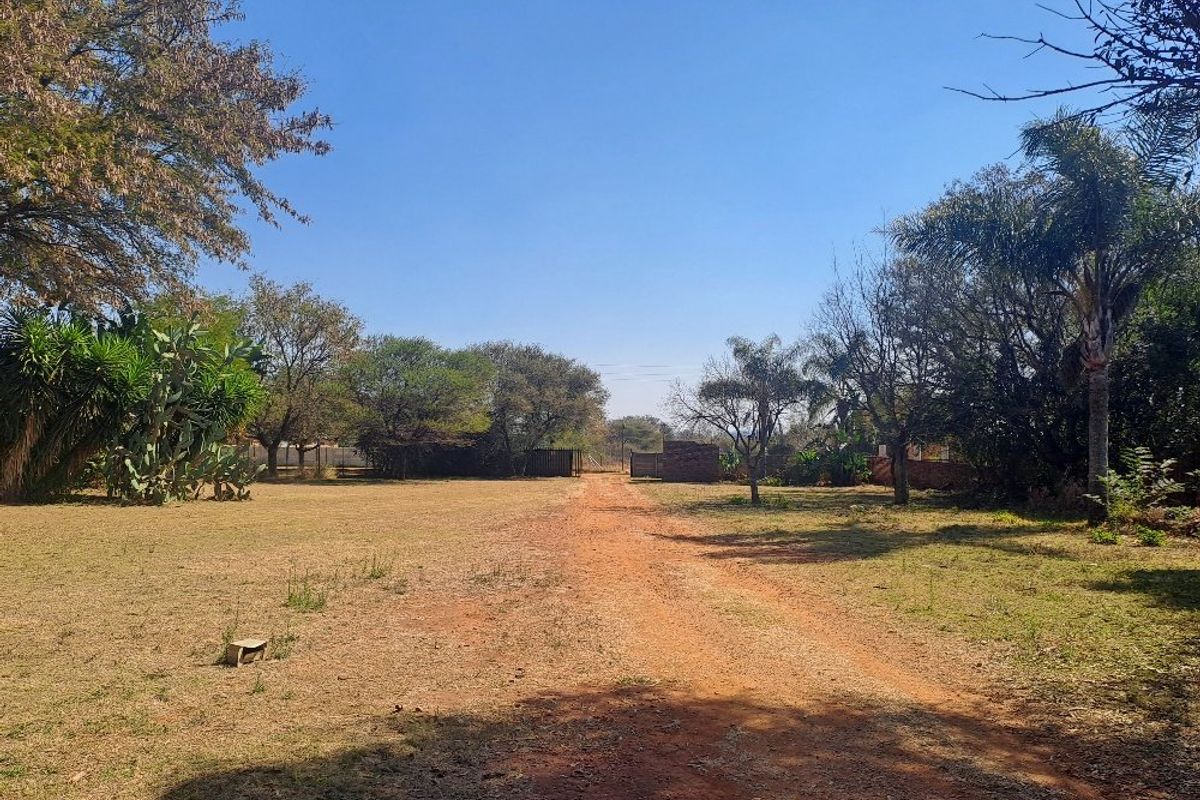 A spacious farm garden featuring a long dirt driveway, mature trees, and established landscaping, providing a natural and open outdoor setting.