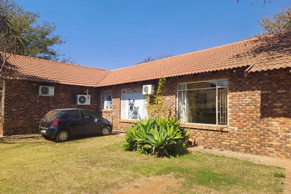 Rear view of a face brick farm-style dwelling featuring a tiled roof, multiple air conditioning units, and secure steel-framed windows overlooking a lawn.