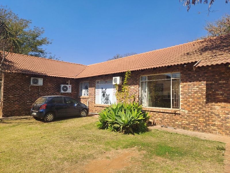 Rear view of a face brick farm-style dwelling featuring a tiled roof, multiple air conditioning units, and secure steel-framed windows overlooking a lawn.