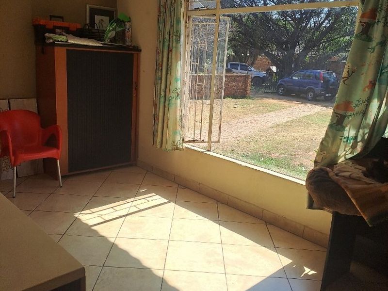 A living area featuring tiled flooring and a large window with security bars, offering natural light and views of the property exterior.