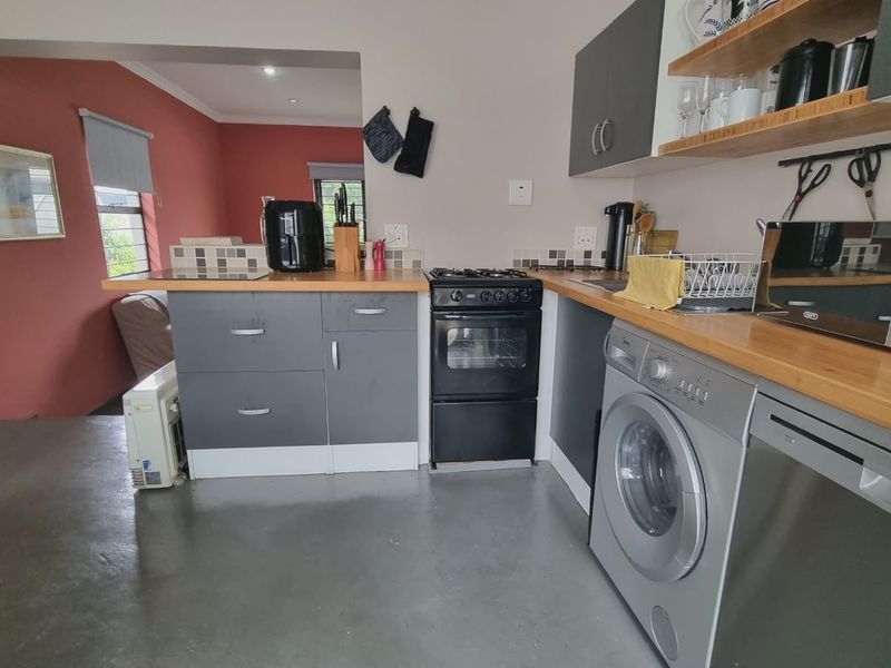 A functional kitchen featuring grey cabinetry, wooden countertops, a gas stove, and integrated laundry and dishwasher appliances.