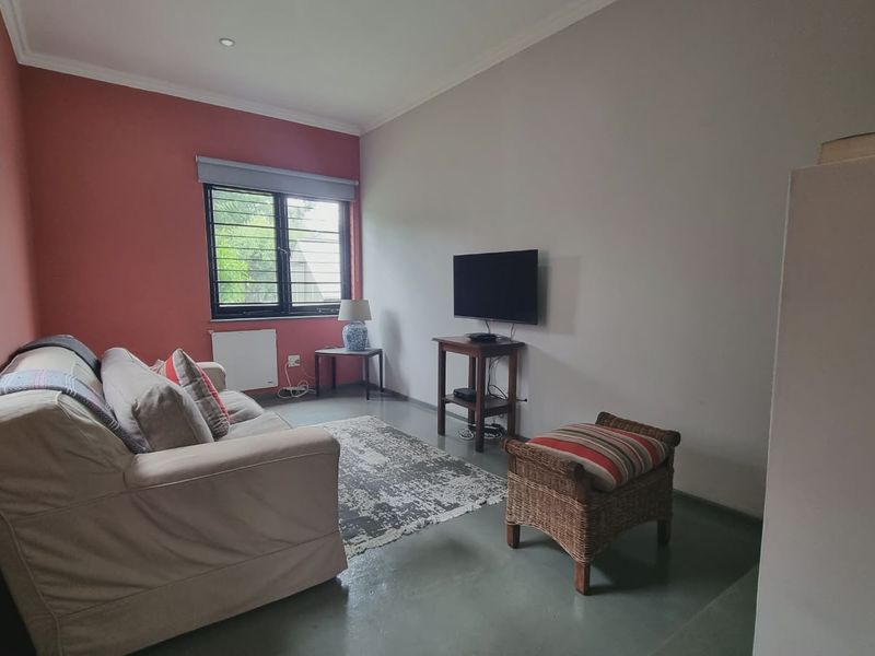 A living room featuring painted accent walls, aluminium window frames, and recessed downlighting, providing a functional and neutral living space.