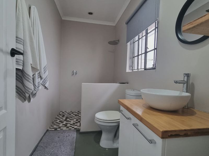 A modern bathroom featuring a vessel sink on a wooden vanity, a walk-in shower area, and a toilet, finished with neutral tones.