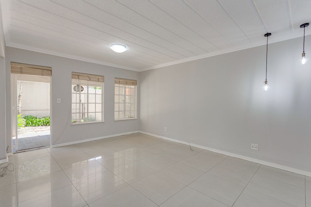 A bright, empty living area featuring neutral tiled flooring, modern pendant lighting, and direct access to an outdoor patio space.