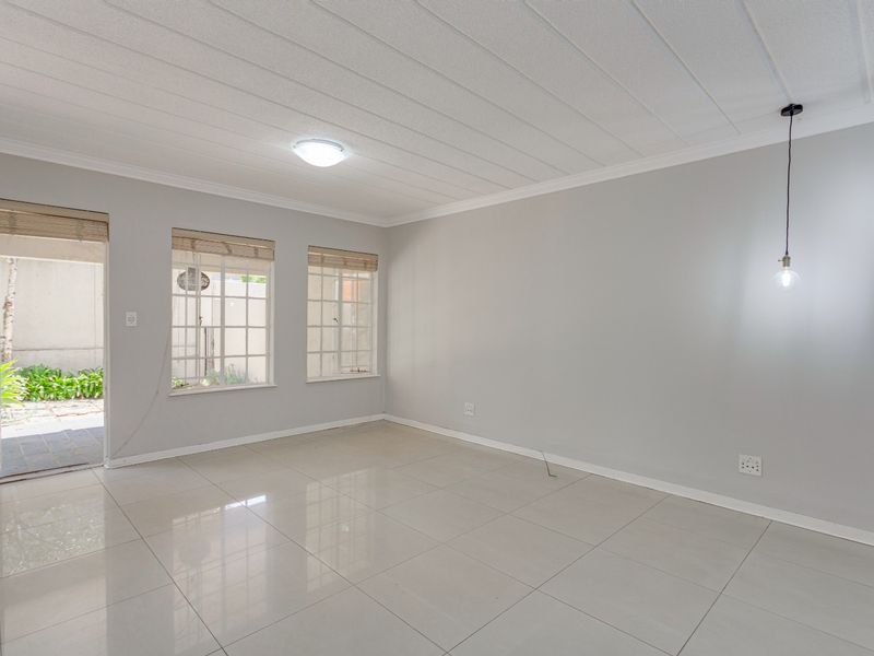 A bright, empty living area featuring neutral tiled flooring, modern pendant lighting, and direct access to an outdoor patio space.