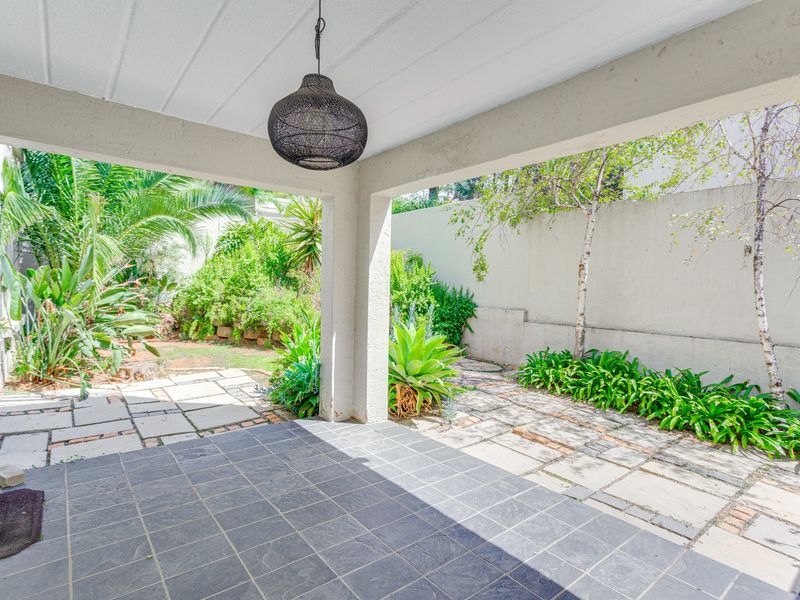 A covered patio area featuring dark tiled flooring, overlooking a private garden with paved pathways and established greenery.