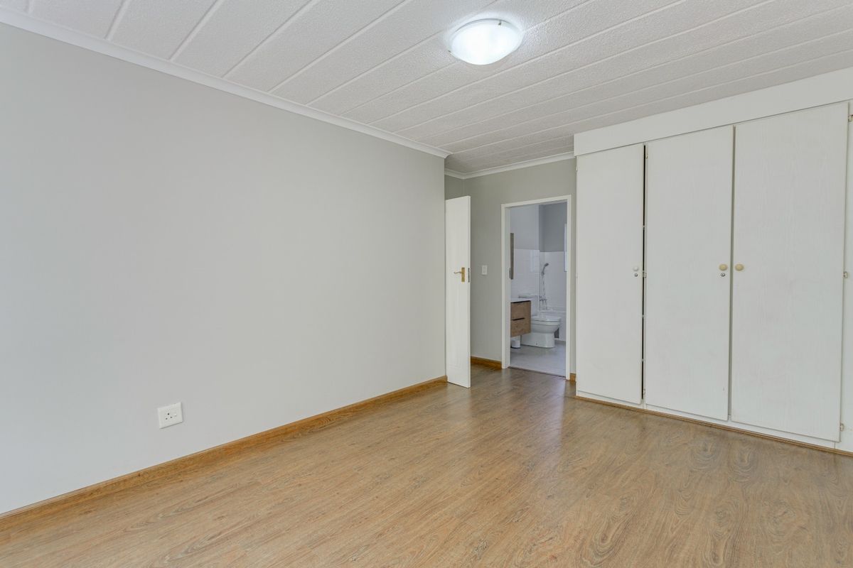 A clean, empty bedroom featuring laminate flooring, built-in cupboards, and direct access to an en-suite bathroom.