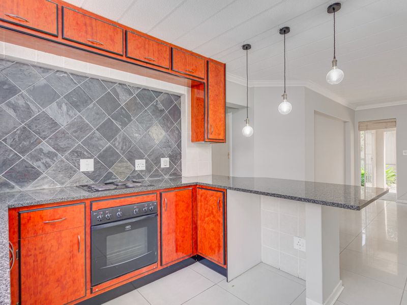 Modern kitchen featuring vibrant wood-finish cabinetry, granite countertops, a slate backsplash, built-in oven, gas hob, and a breakfast bar with pendant lighting.