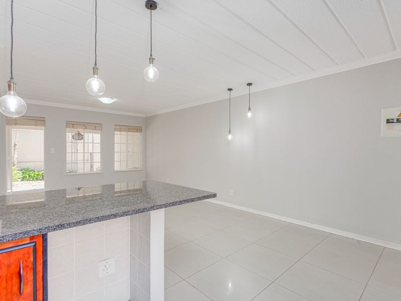 An open-plan living and kitchen area featuring a granite-topped island, neutral tiled flooring, and modern pendant lighting in a bright, vacant space.